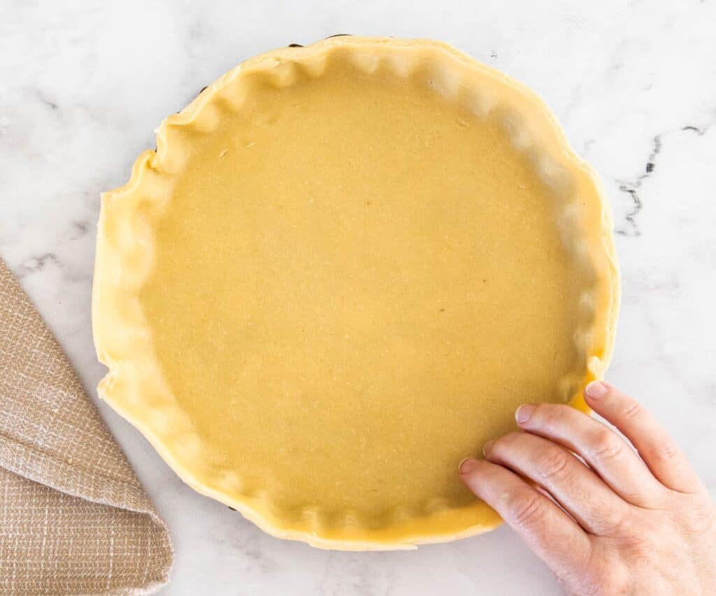 Pastry being pressed into a fluted tart pan.