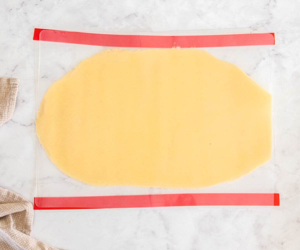The pâte sablée dough rolled out between two silicone sheets with red rolling guides on the top and bottom