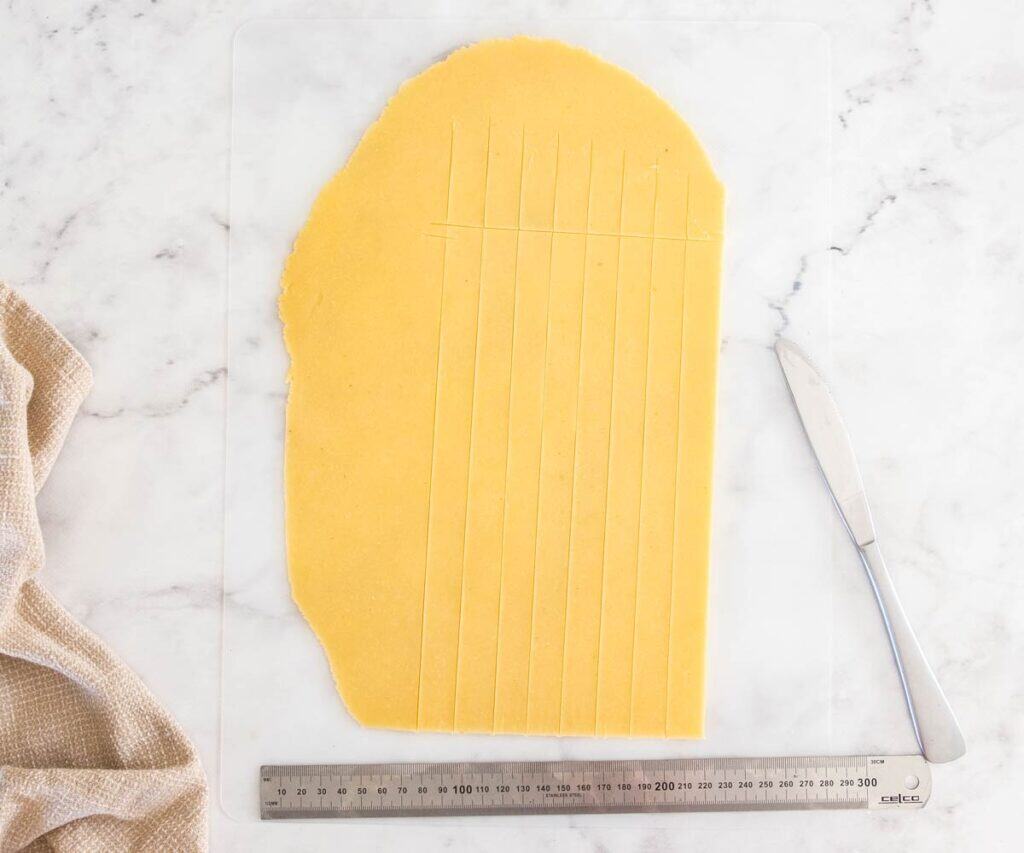 A sheet of pâte sablée dough with strips cut from it.