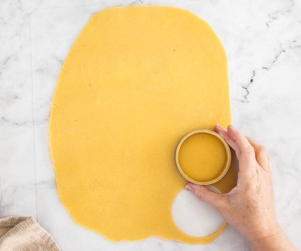 A hand holding a tart ring and pressing it into pastry dough to cut out a circle.