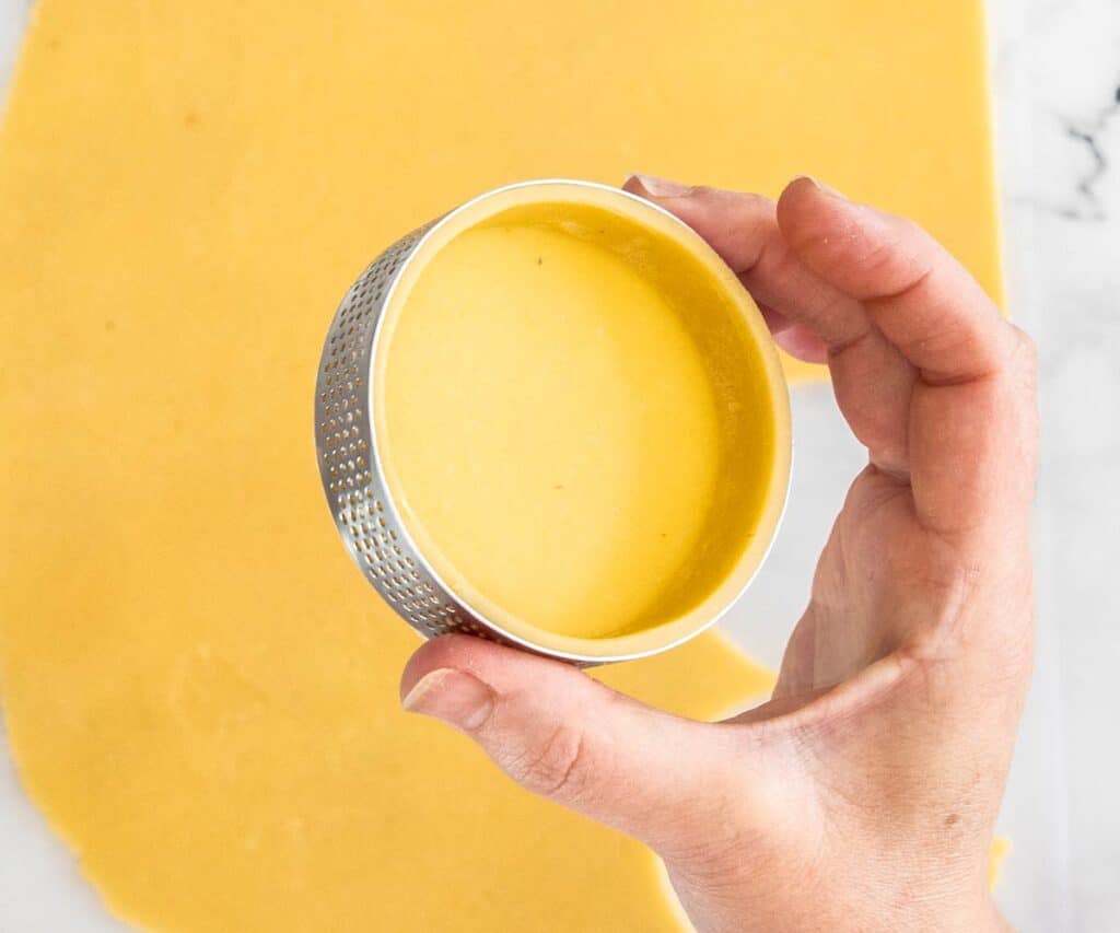 Closeup of a pâte-sablée tart shell in a perforated tart ring before baking.