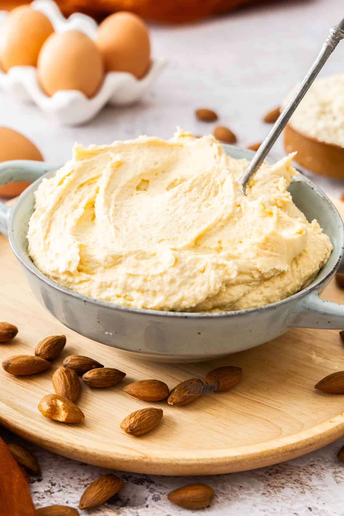 A bowl filled with almond cream with eggs in the background and almonds in the foreground.