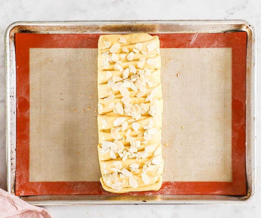 The proofed Danish almond braid on a baking sheet topped with sliced almonds, ready to bake.