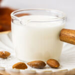 Closeup of a glass jug filled with almond glaze with whole almonds in front.