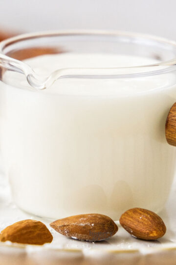 Closeup of a glass jug filled with almond glaze with whole almonds in front.