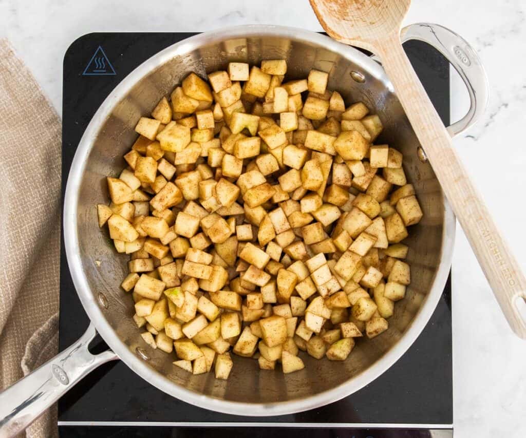 Apples mixed with cinnamon in a pan.
