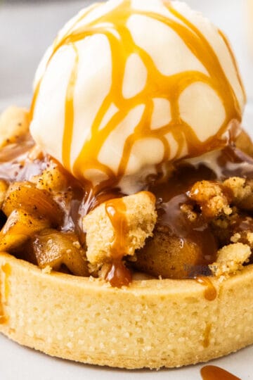 Extreme closeup of an apple crumble tartlet topped with ice cream and caramel sauce.