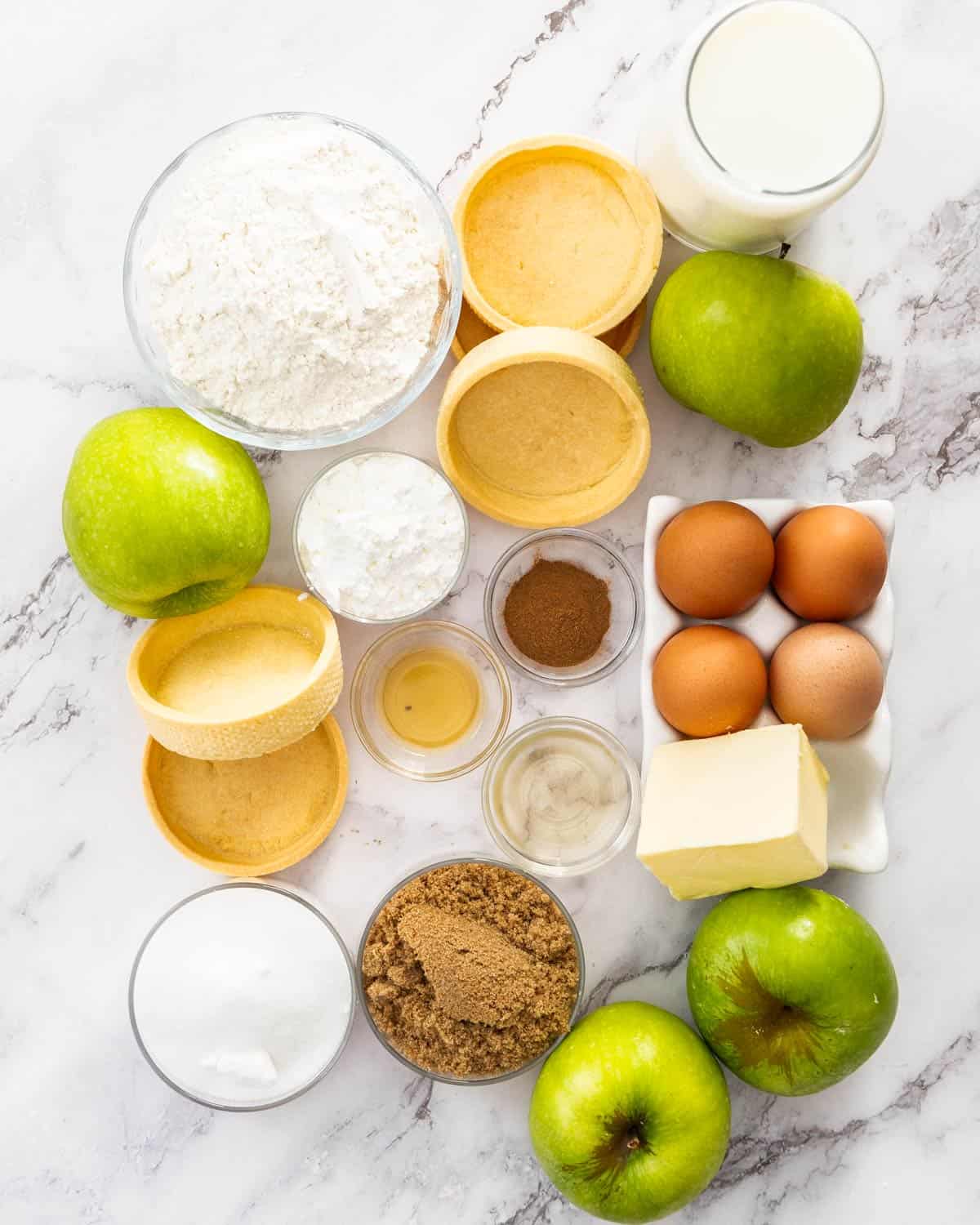 Ingredients for apple crumble tartlets on a marble surface.