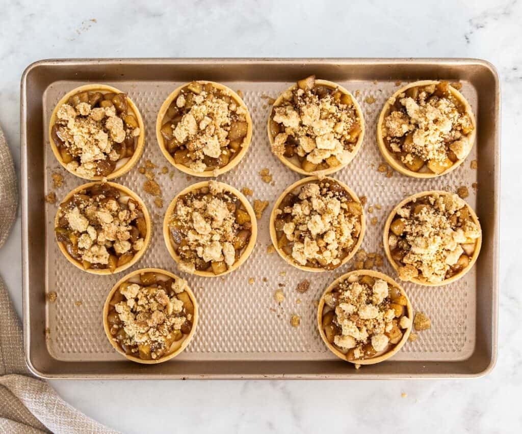 10 apple crumble tartlets on a baking tray.