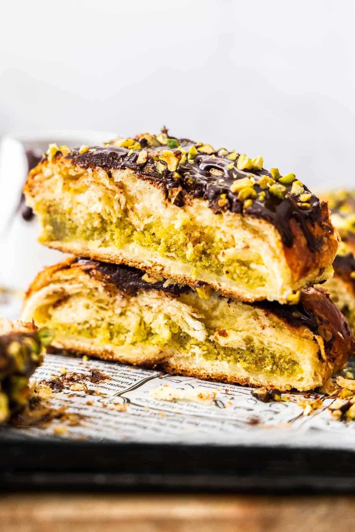 Two slices of pistachio Danish braid topped with chocolate glaze stacked.