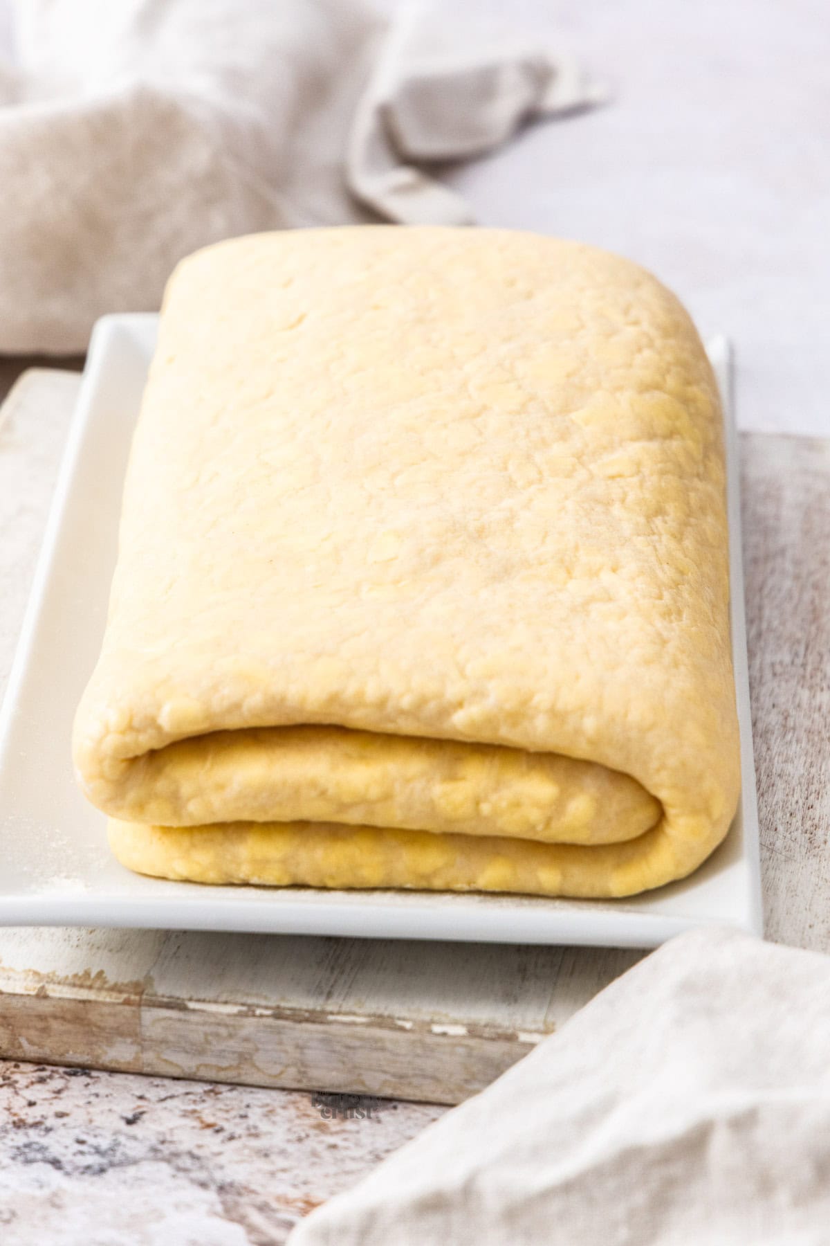 A block of folded Danish dough, proofed in the fridge overnight on a plate.