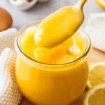 A spoon lifting lemon curd out of a glass jar.