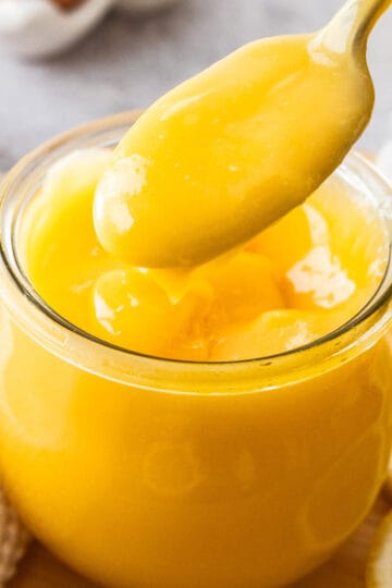 A spoon lifting lemon curd out of a glass jar.