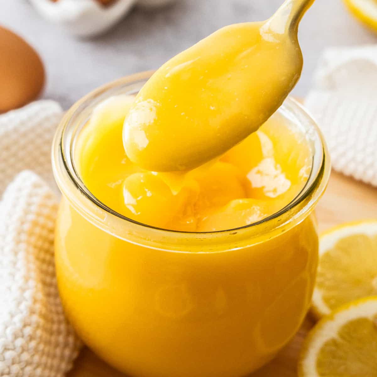 A spoon lifting lemon curd out of a glass jar.