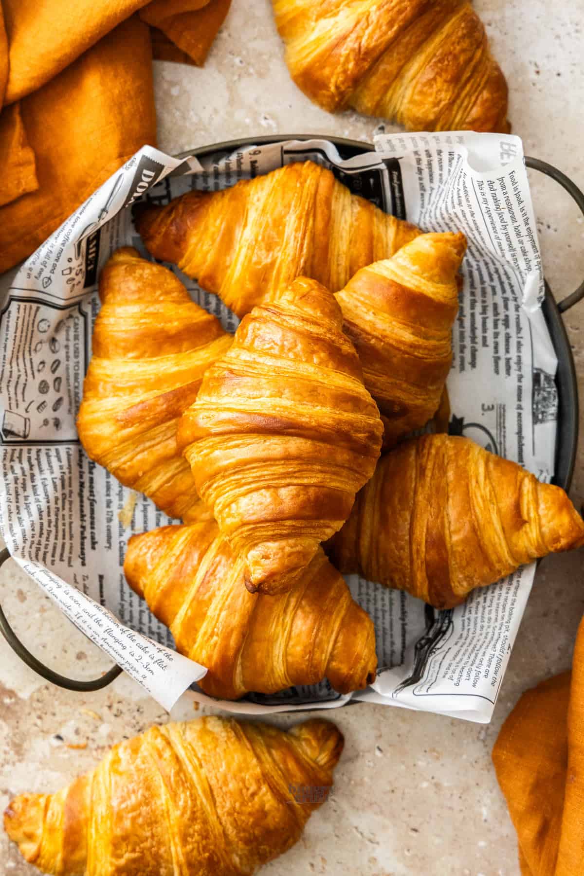 Top down view of 6 golden, flaky croissants in a metal tray.