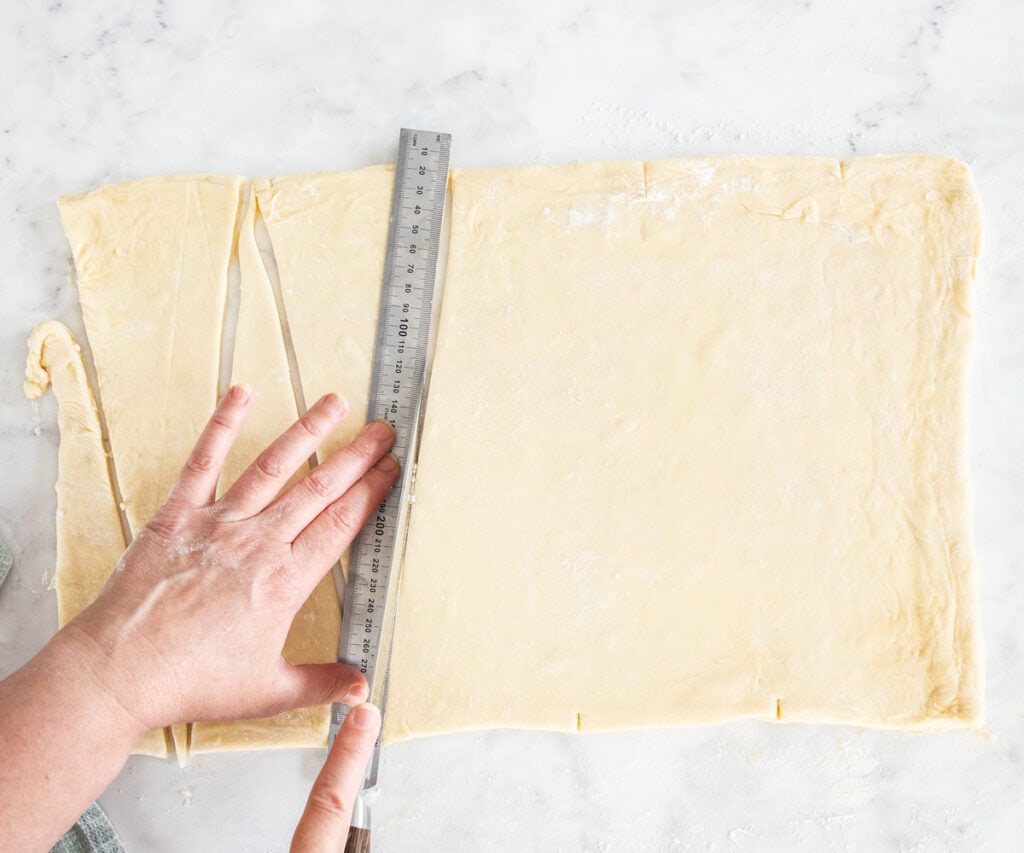 A ruler on the dough and a knife slicing to show how to cut the dough into croissant triangles.