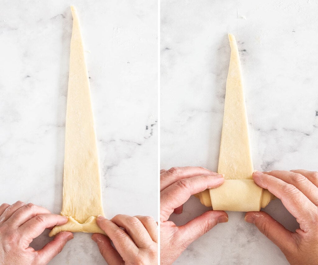 Two hands rolling the dough triangle up into a croissant.