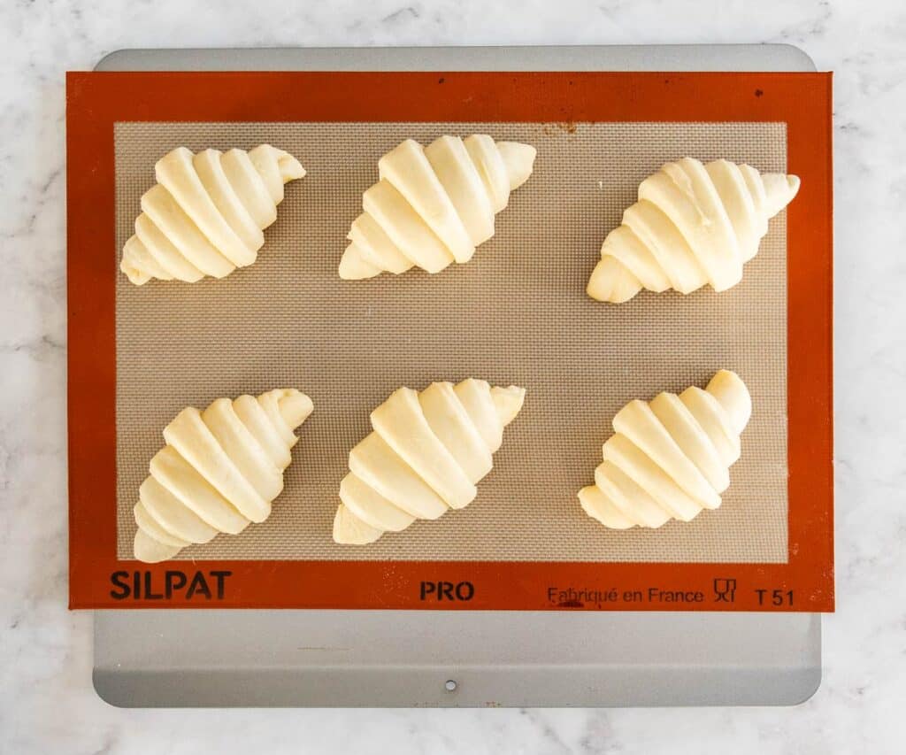 Six croissants on a baking sheet looking puffy and ready to bake.