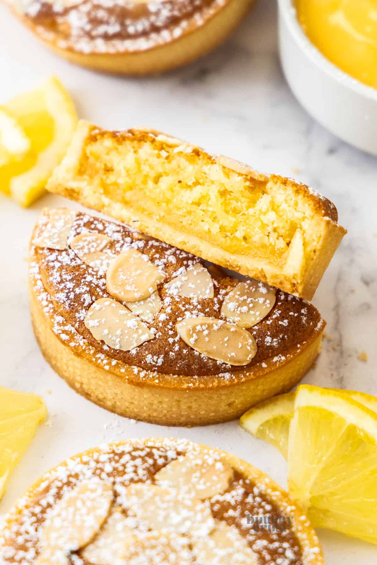 A lemon almond tart sliced in half to show the lemon curd and almond filling inside.