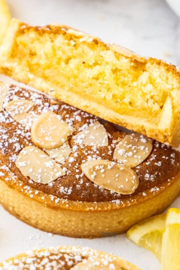 A lemon almond tart sliced in half to show the lemon curd and almond filling inside.