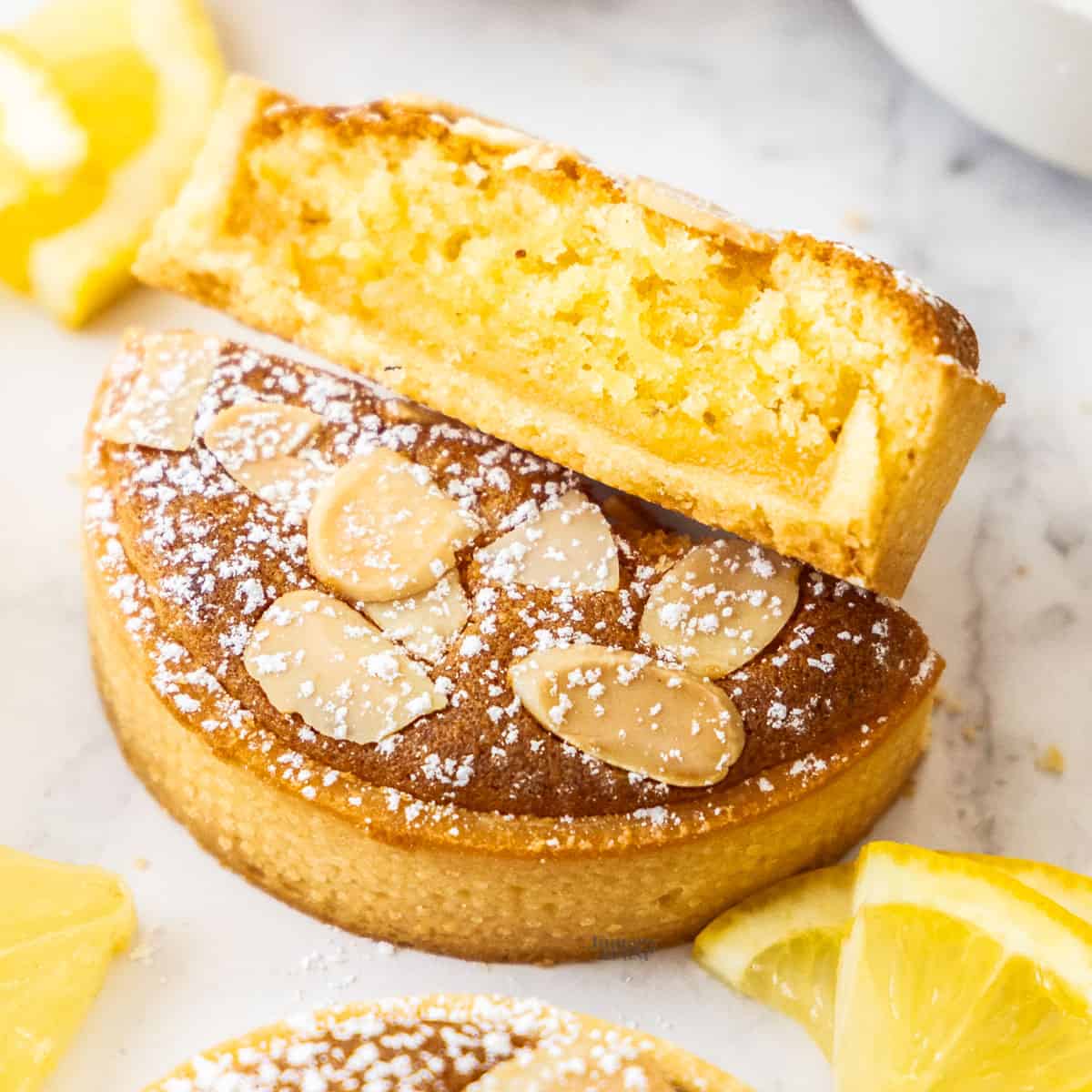 A lemon almond tart sliced in half to show the lemon curd and almond filling inside.