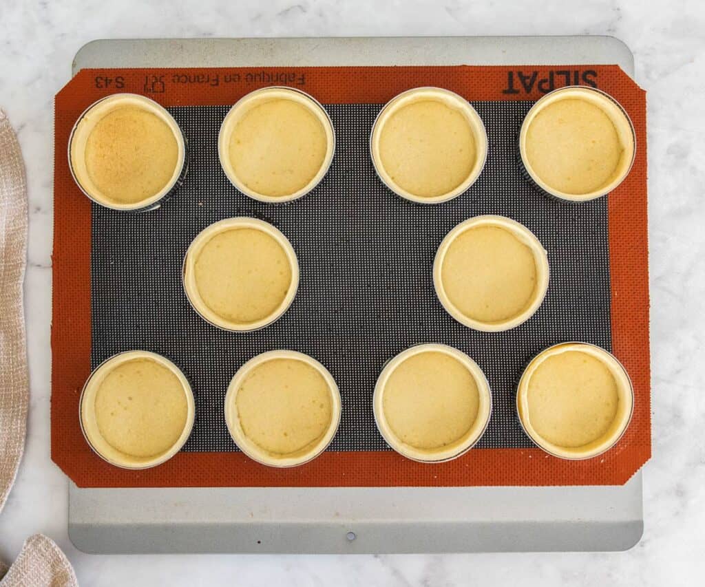 10 parbaked tart shells on a baking sheet.
