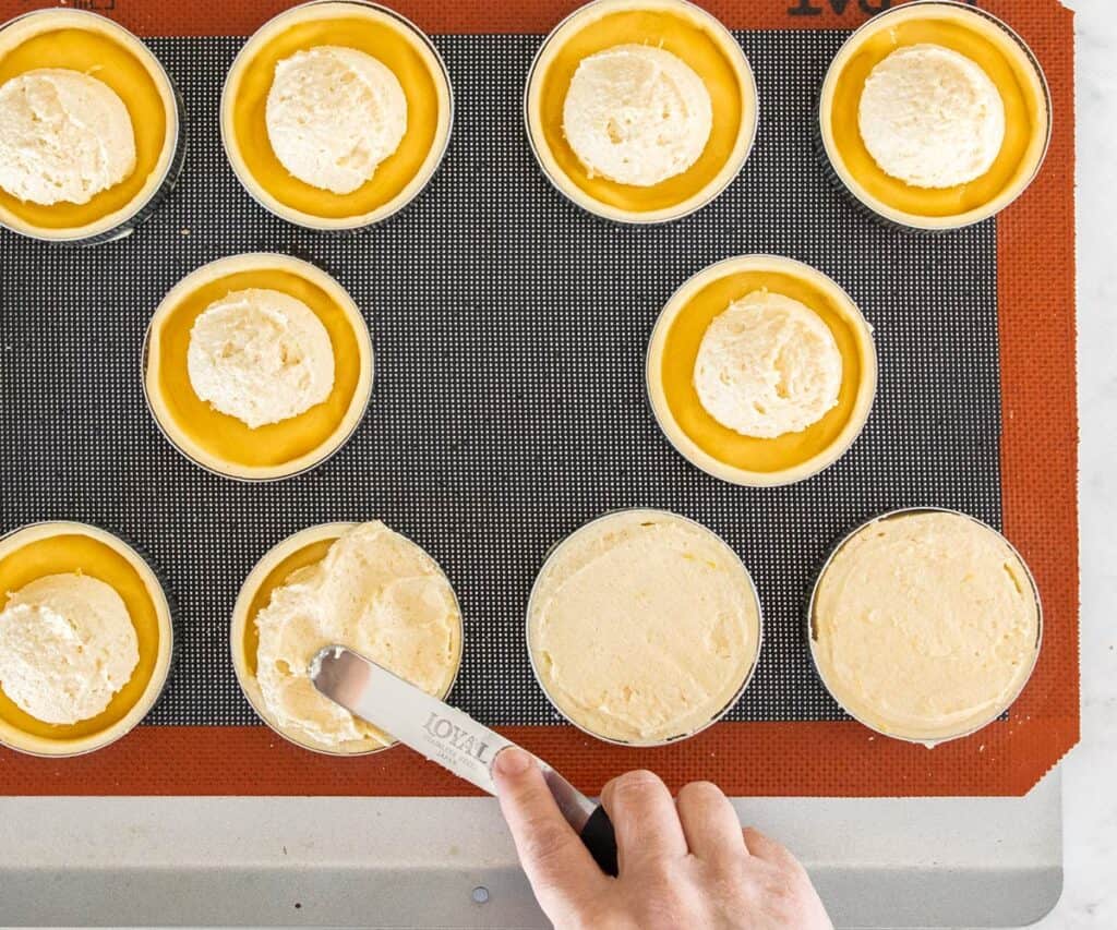 Almond frangipane being spread over lemon curd in the tart shells.