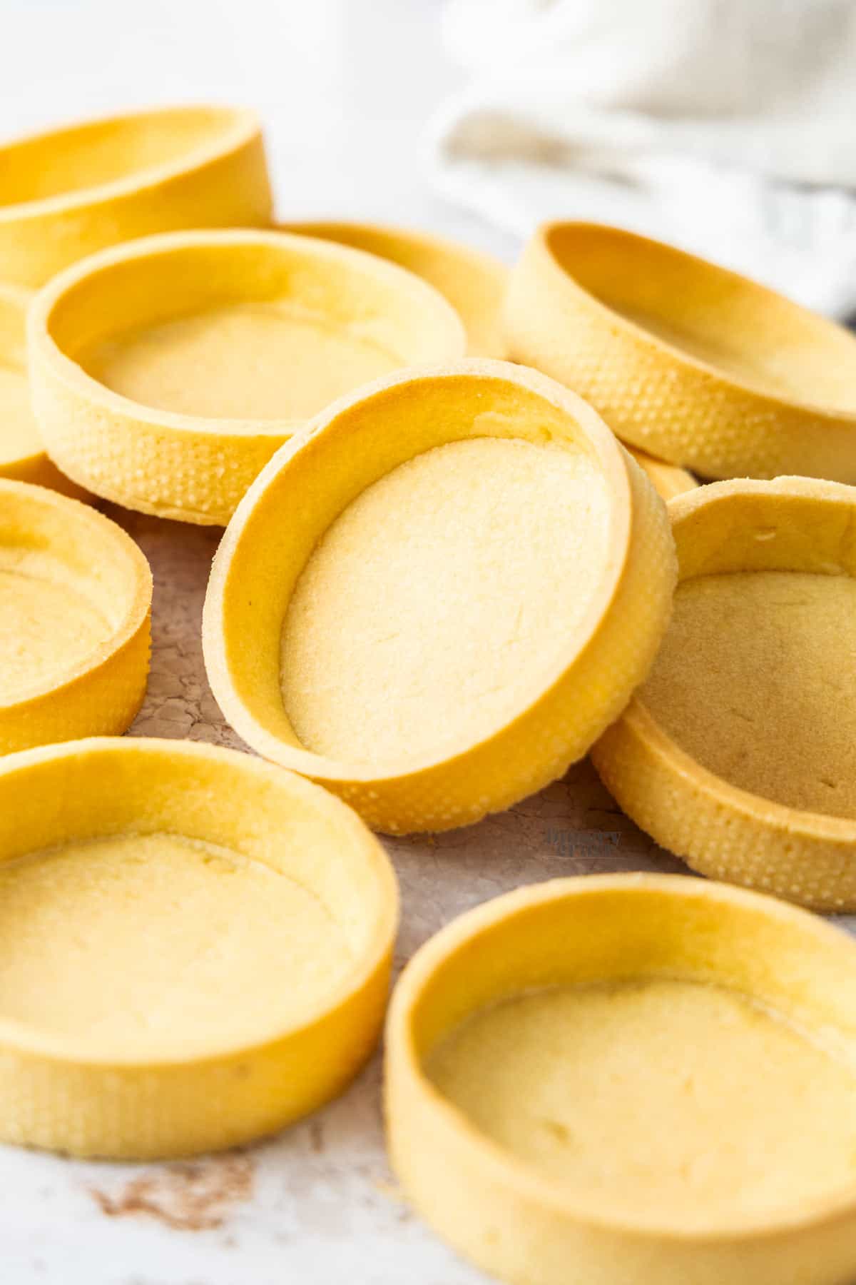 A batch of pâte sablée tart shells with one on an angle.