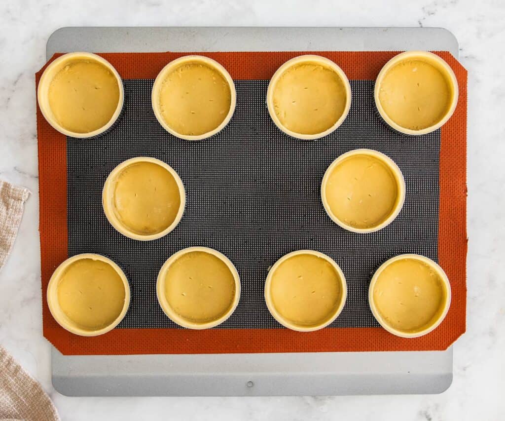 10 raw tart shells on a baking tray ready to bake.