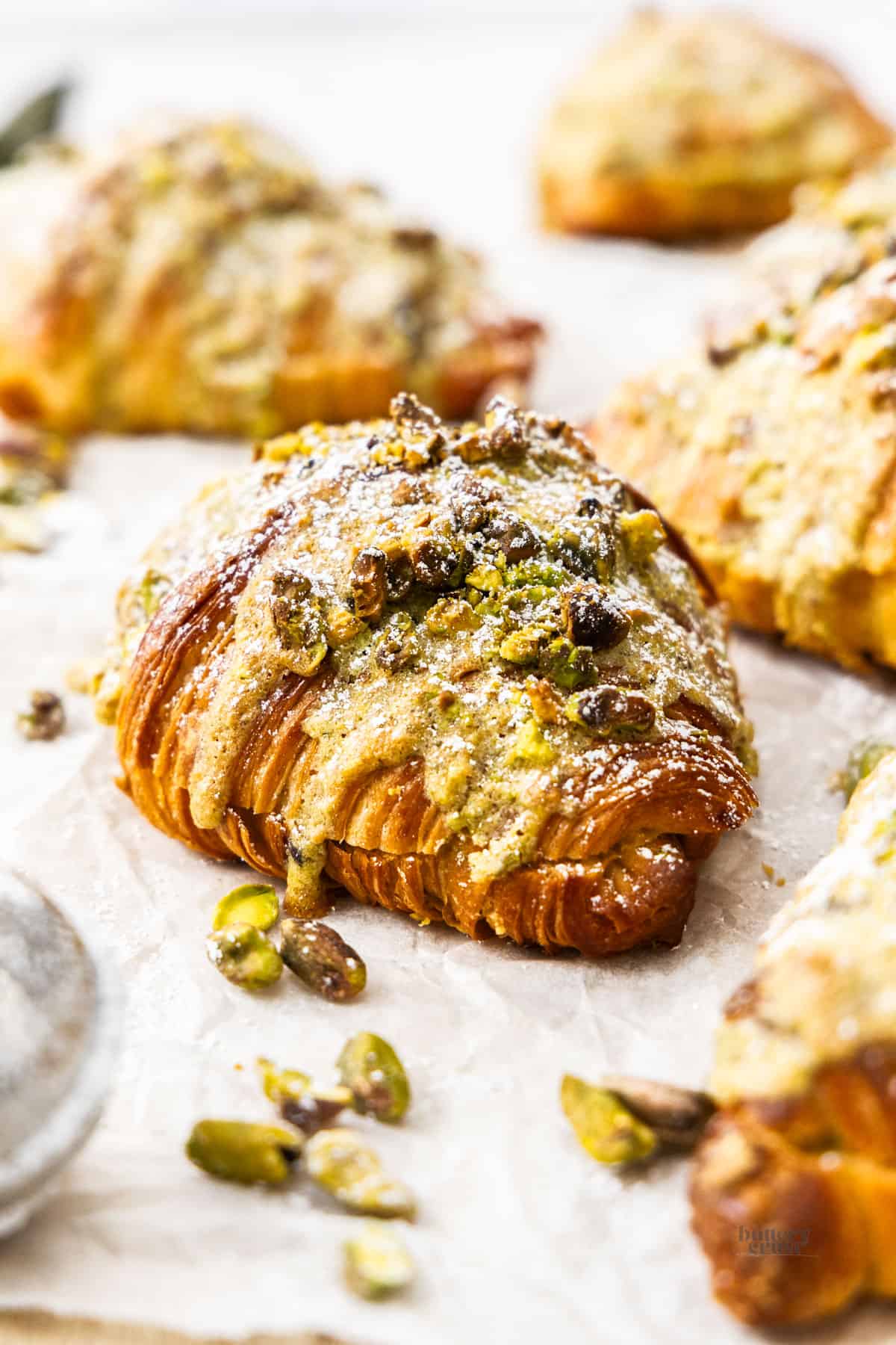 Closeup of a pistachio croissant with pistachios scattered around.