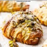Closeup of a pistachio croissant with pistachios scattered around.