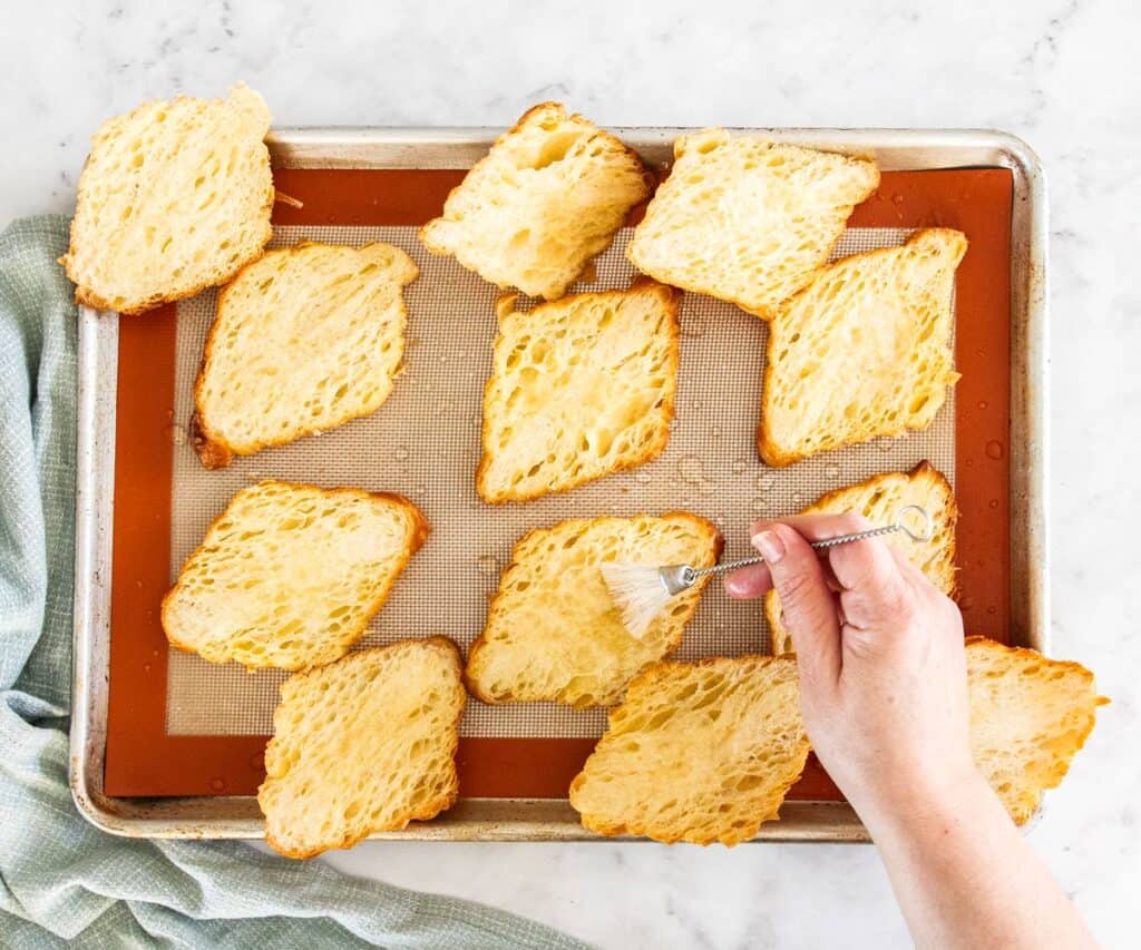 Croissants cut in half on a baking tray being brushed with syrup.