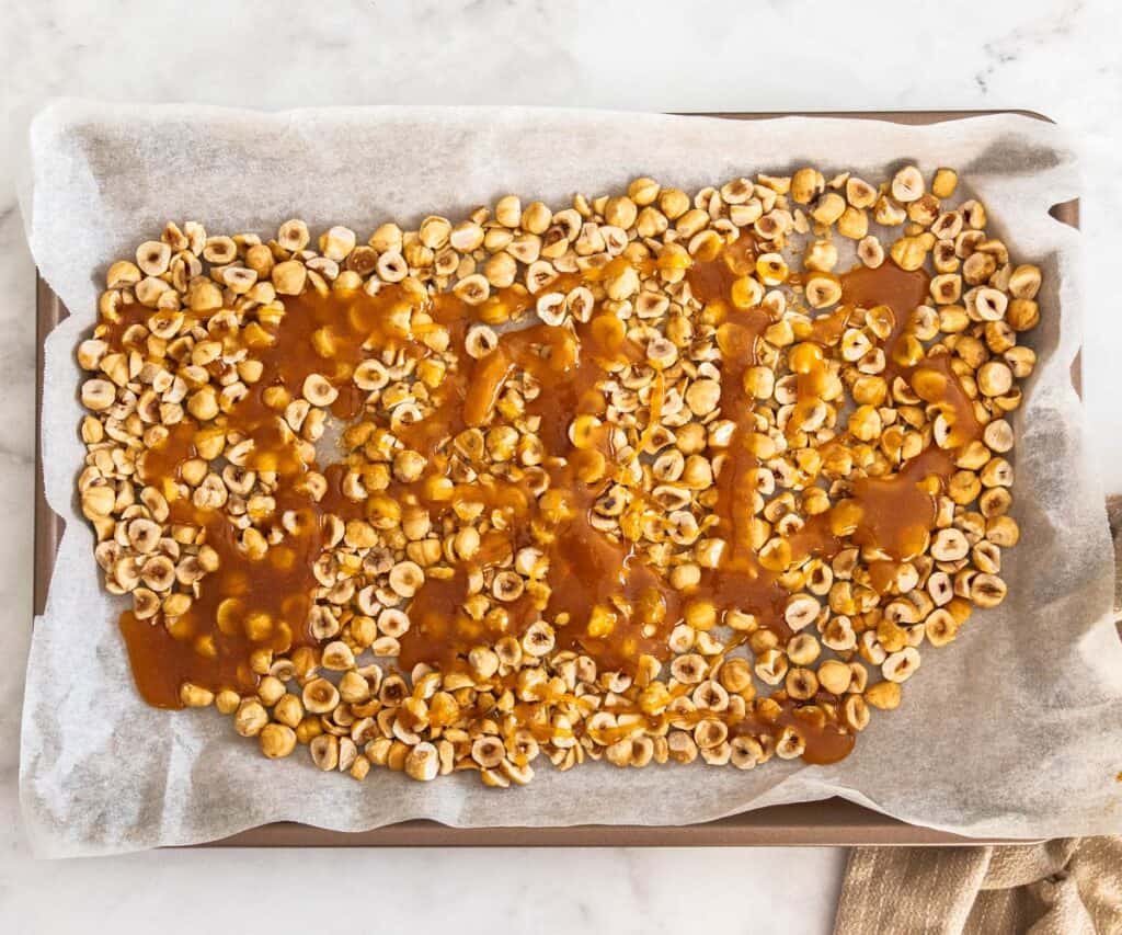 The caramel poured over hazelnuts on a baking tray.