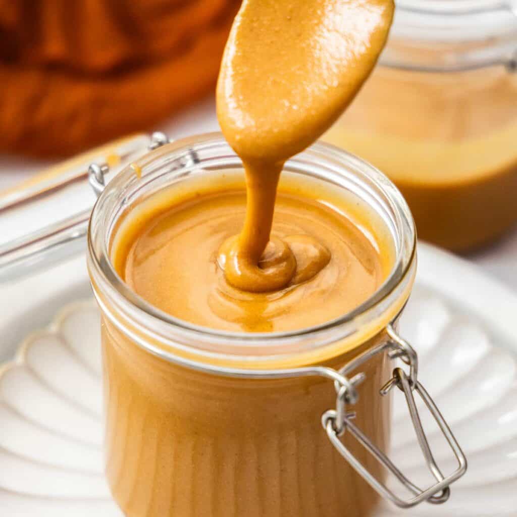 A spoon drizzling praline paste into a glass jar.