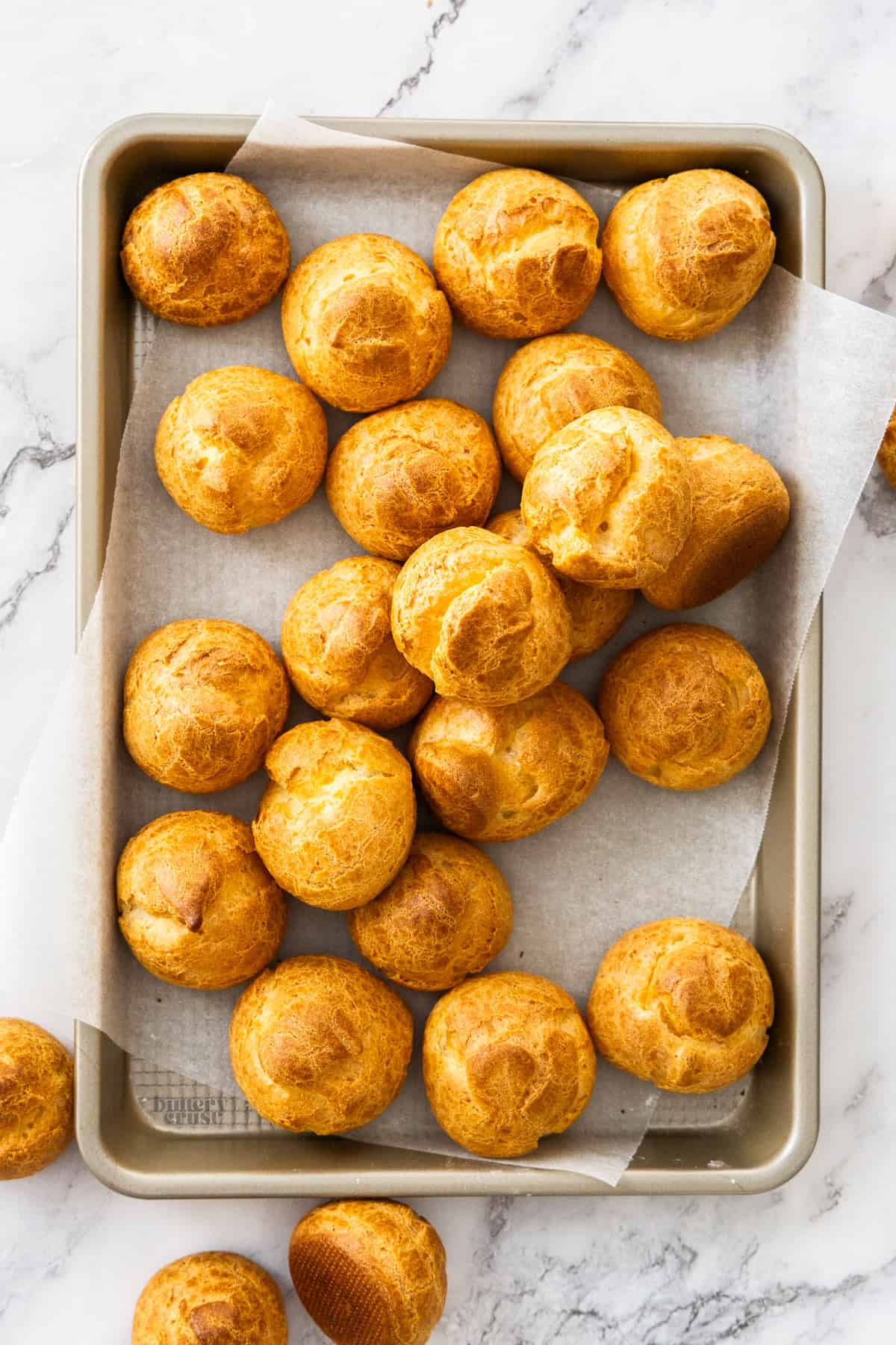 Top down view of a batch of choux buns on a metal tray.