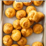 Top down view of a batch of choux buns on a metal tray.