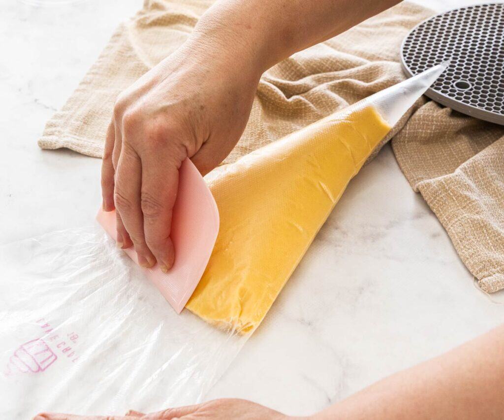 Using a dough scraper to press the choux pastry dough into the piping bag.