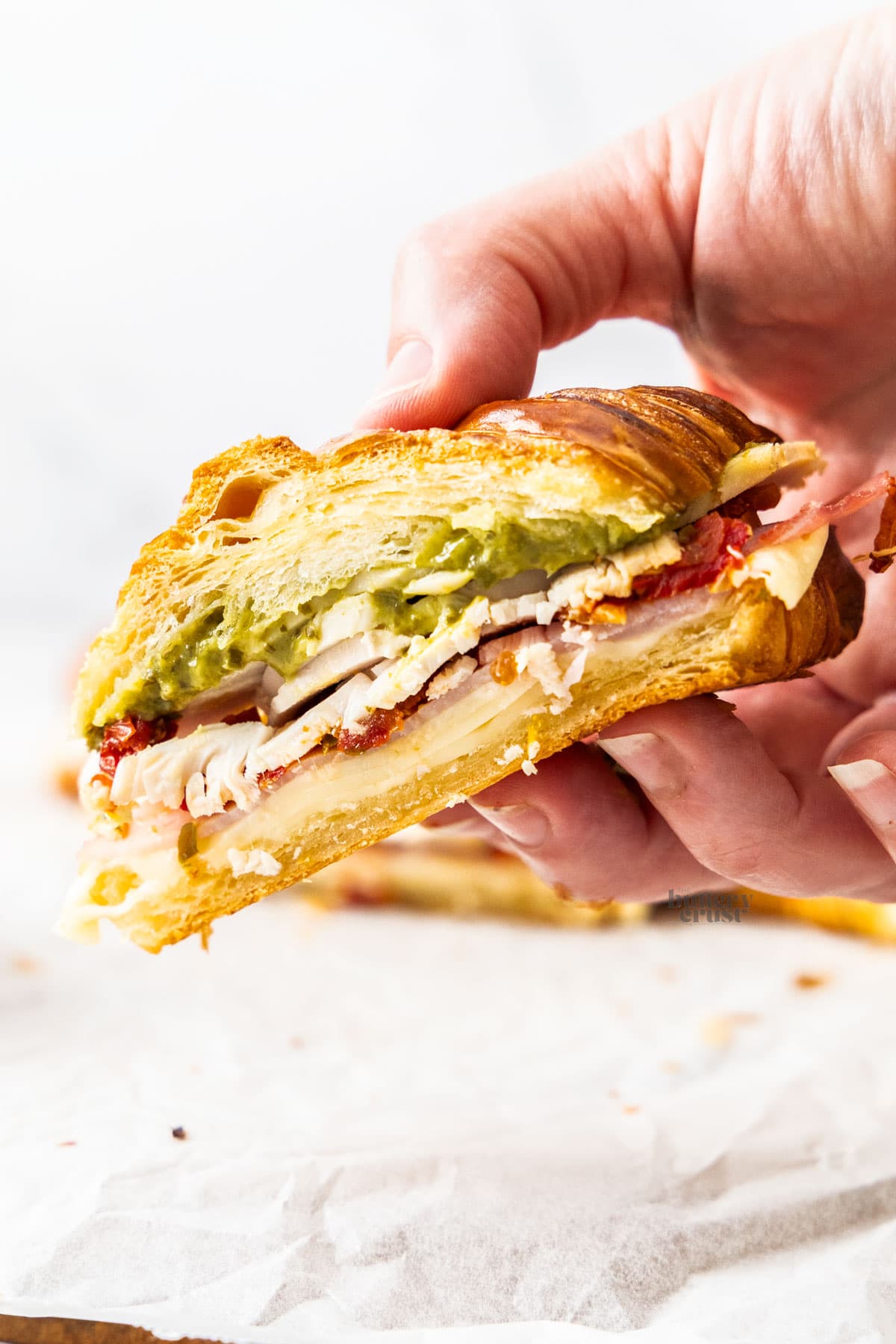 A hand holding half of a turkey croissant sandwich.
