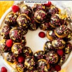 Top down view of profiteroles in a wreath shape decorated with chocolate and gold leaf.