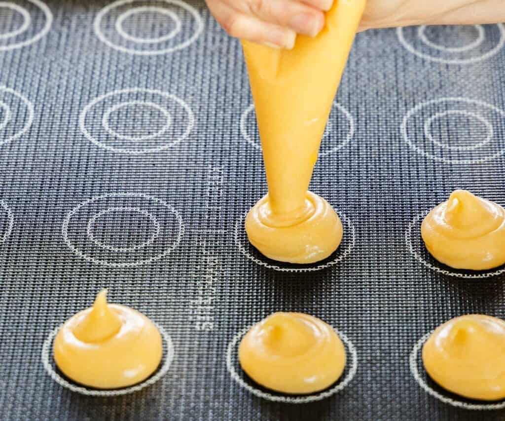 Piping choux pastry onto a baking sheet.