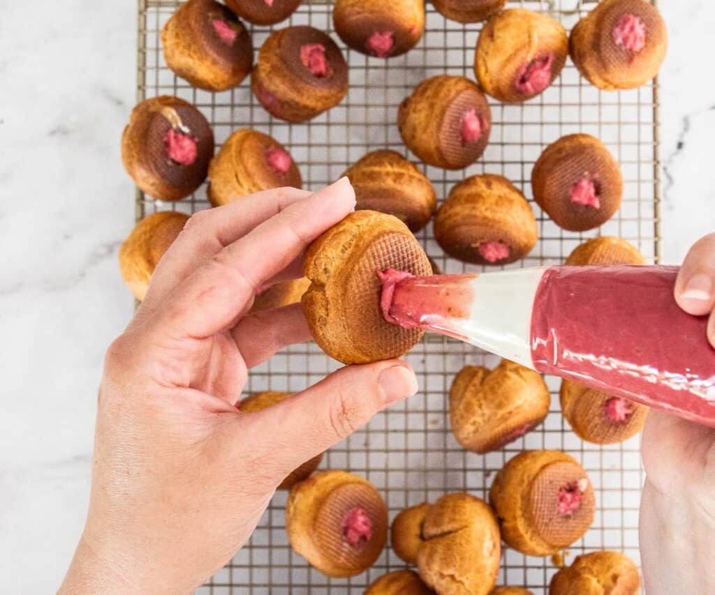 Piping raspberry pastry cream into choux buns.