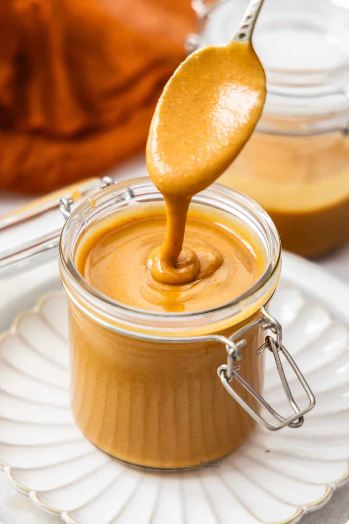 Hazelnut praline paste dribbling off a spoon into a jar.