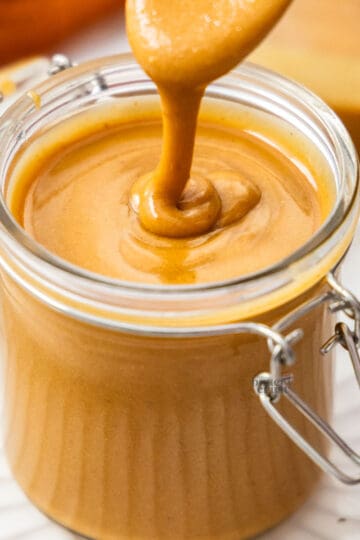 Hazelnut praline paste dribbling off a spoon into a jar.