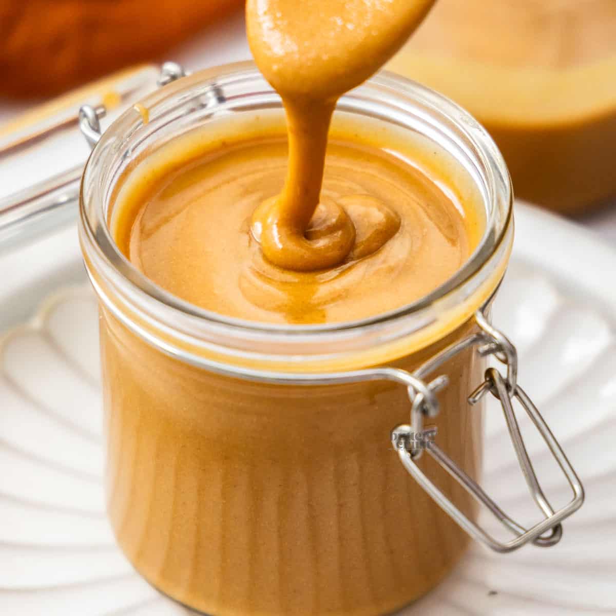 Hazelnut praline paste dribbling off a spoon into a jar.