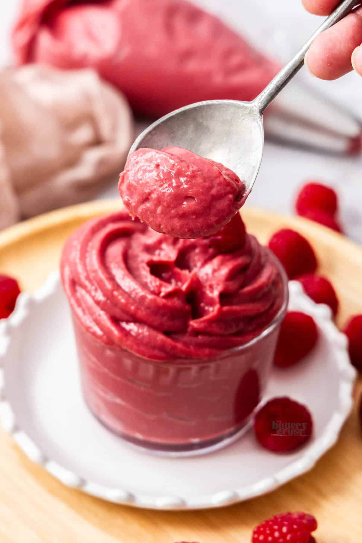 A spoon taking some raspberry pastry cream from a glass.