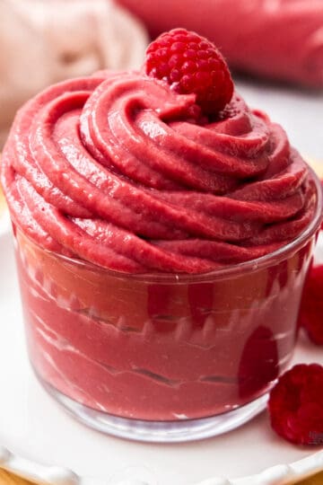 Raspberry pastry cream piped into a glass with a raspberry on top.