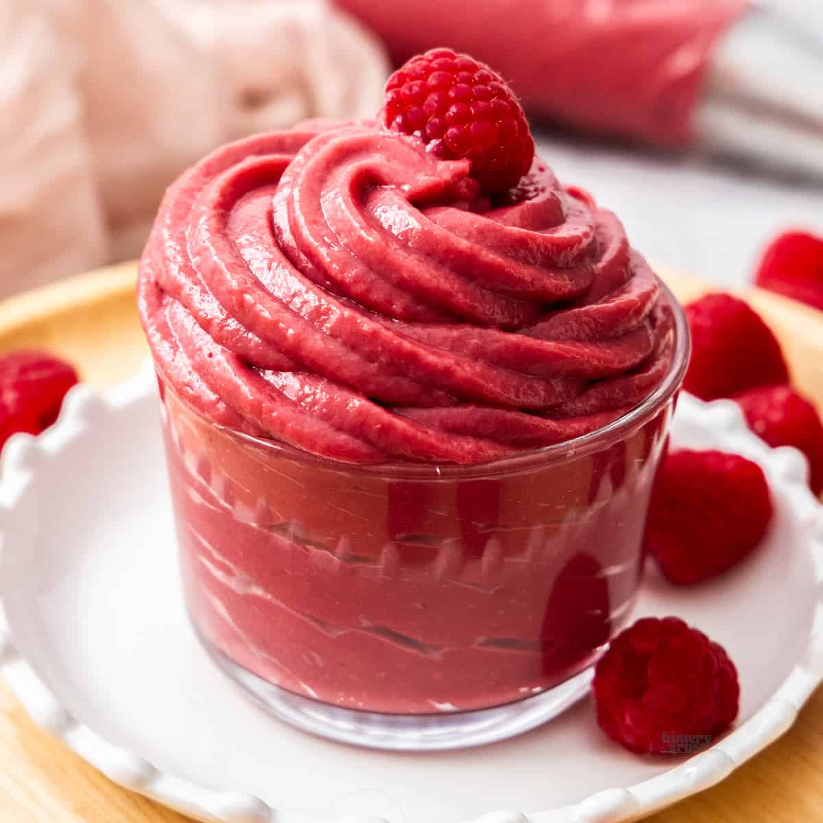 Raspberry pastry cream piped into a glass with a raspberry on top.
