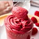 A spoon taking some raspberry pastry cream from a glass.