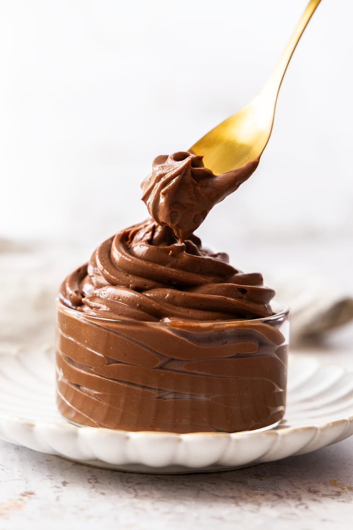 A spoon taking some chocolate pastry cream from a glass dish.