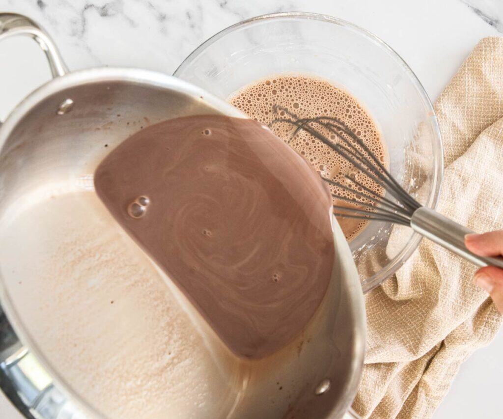 Pouring the hot chocolate milk into a bowl of whisked eggs and cornflour.